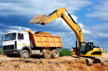 Excavator loading dumper truck tipper in sand pit over blue sky